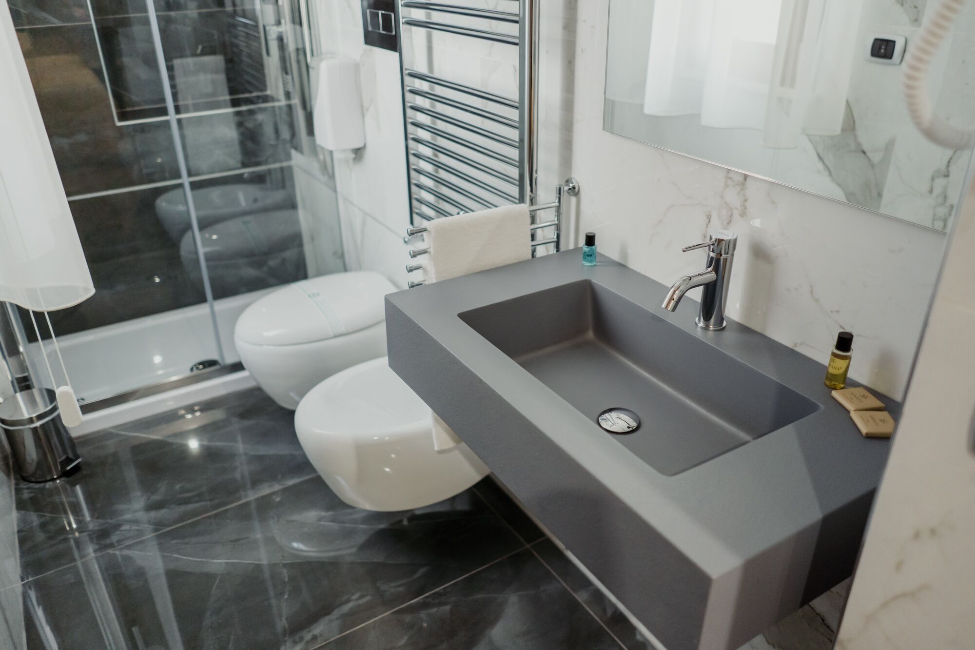 Une salle de bain moderne avec un lavabo gris, des toilettes blanches et une douche à parois de verre.