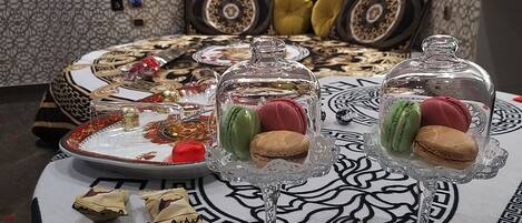Una mesa de comedor con dos exhibidores de vidrio para postres, cada uno con macarons, y un plato con un objeto decorativo.