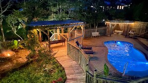 Una terraza de madera con piscina, rodeada por una valla de madera y una zona cubierta con asientos.