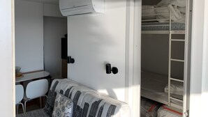 Ett litet rum med en våningssäng, ett litet skrivbord med en stol och en vit luftkonditioneringsenhet som är monterad på väggen.