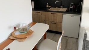 Ett kompakt kök med träskåp, en mikrovågsugn, ett handfat och ett litet kylskåp. Det finns ett matbord med två stolar och en dekorativ skål på bordet.