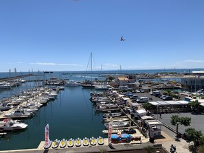 A marina with multiple boats docked, a clear sky, and a distant bridge. - Vue magnifique du vieux port Studio cabine - A/C - Wifi - parking (Agde)