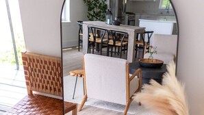 Una sala de estar moderna con un banco de madera, una silla y un espejo grande que refleja una cocina.