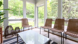 Una habitación soleada con ventanas amplias, sillas de mimbre, una mesa y una planta en maceta.