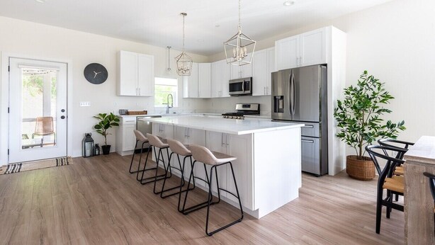 Una cocina moderna con armarios blancos, electrodomésticos de acero inoxidable, una isla central con taburetes de bar e iluminación colgante.