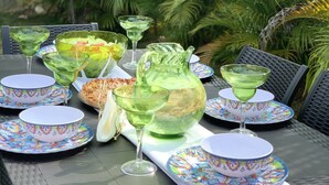An outdoor dining table set with colorful plates, green glassware, and a pitcher, surrounded by lush greenery. - Beautiful Full House Rental in Private Gated Community,  Montego Bay, Jamaica (Montego Bay)