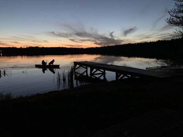 Un paysage paisible au bord d’un lac, avec une jetée en bois s’étendant dans des eaux calmes, entouré d’arbres et sous un ciel dégagé.