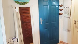 Eine blaue Tür mit weißem Rahmen, eine Holztür zur Linken, eine Wandleuchte und ein Schild mit positiven Botschaften.