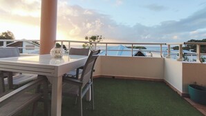 Ein Balkon mit Tisch und Stühlen, einer Ziervase und Blick auf das Meer und Gebäude.