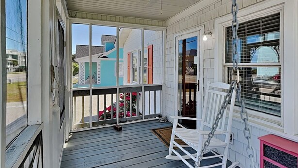 A covered porch with a rocking chair, a small table, and a window with blinds. - Good Vibrations | Pet-friendly w/ Beach Views (Carolina Beach)