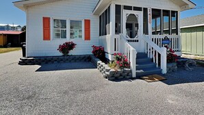 A single-story house with a porch, a front door, and a small garden with red flowers. - Good Vibrations | Pet-friendly w/ Beach Views (Carolina Beach)