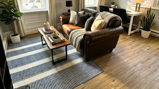 A living room with a brown leather sofa, a coffee table, a rug, and a painting on the wall. - The Grayson at Park Place - Historic Charm Meets Modern Comfort (Wilmington)