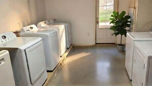 A laundry room with four white washing machines, a potted plant, and a door leading outside. - The Grayson at Park Place - Historic Charm Meets Modern Comfort (Wilmington)