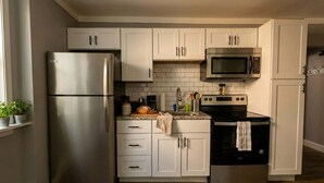 A compact kitchen with white cabinets, a stainless steel refrigerator, a microwave, and an oven. - The Grayson at Park Place - Historic Charm Meets Modern Comfort (Wilmington)