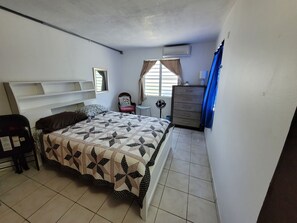 Une chambre à coucher comprenant un lit, une commode, une chaise, un bureau et une fenêtre avec des rideaux.