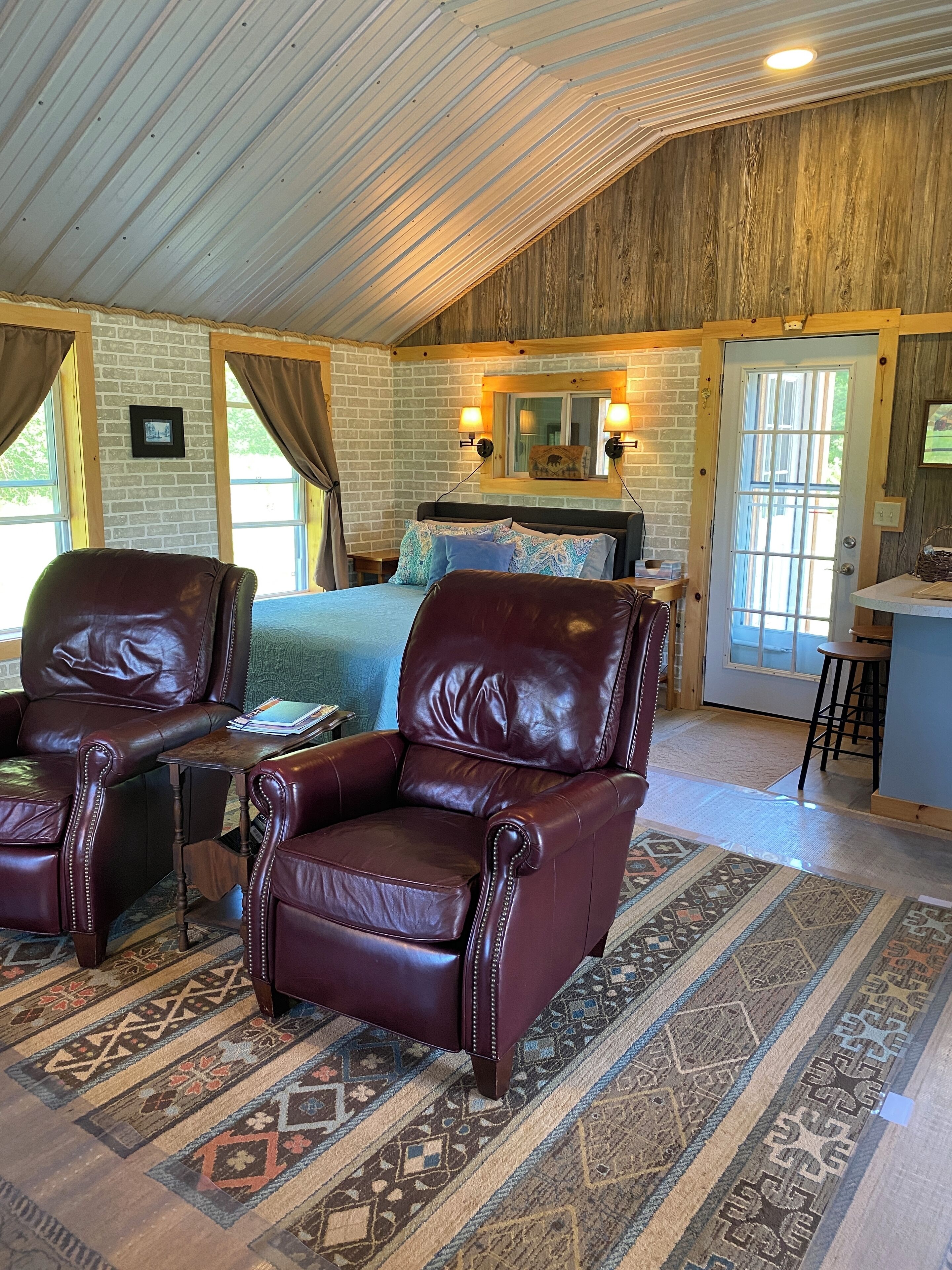 Une pièce confortable avec un lit, deux fauteuils en cuir, une petite table et un tapis à motifs.