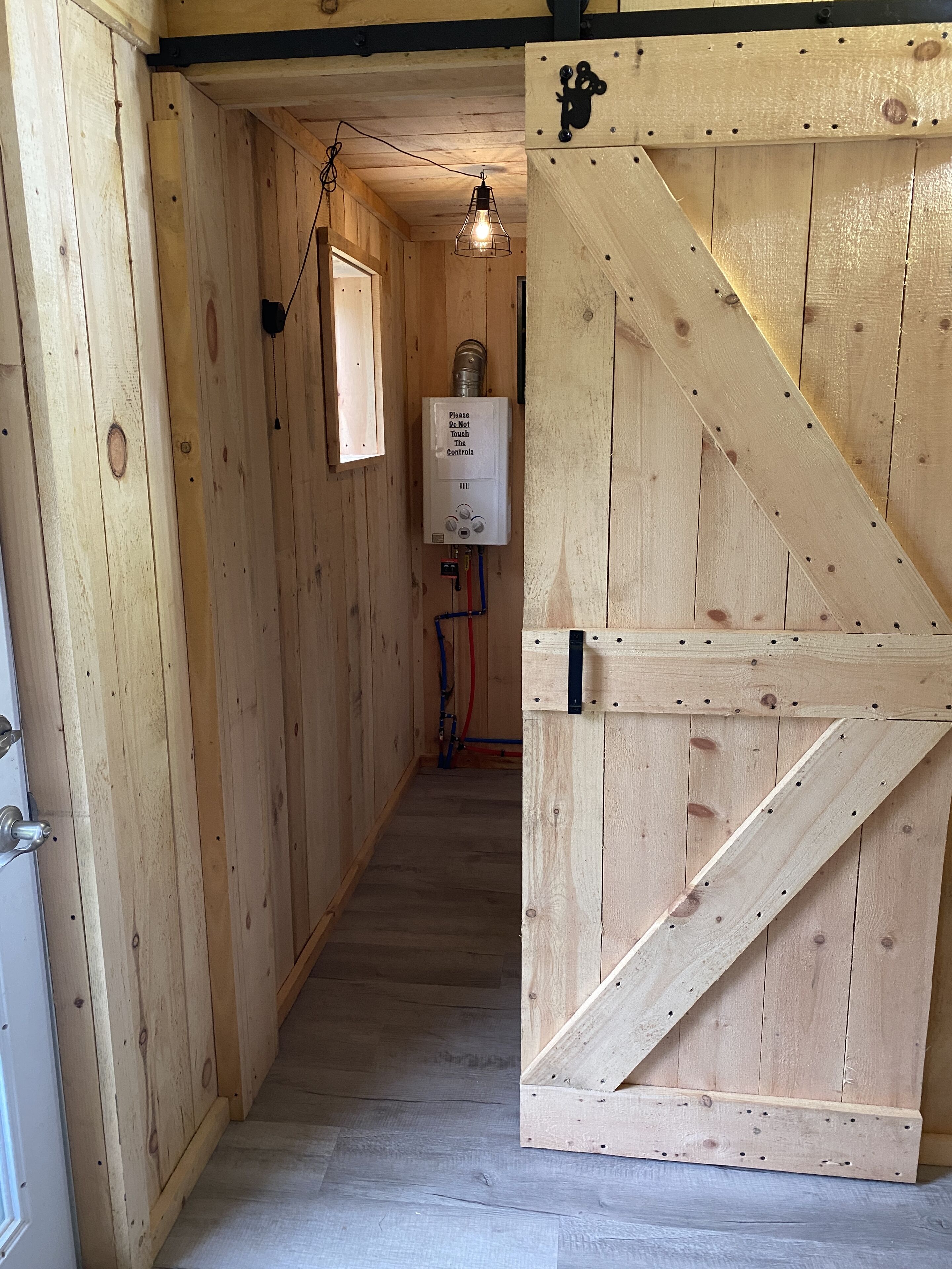 Un couloir en bois avec une grande porte de style grange, un chauffe-eau apparent et un luminaire suspendu.