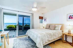 Relax in this serene bedroom with a large bed, ceiling fan, and sliding glass door leading to an ocean view.