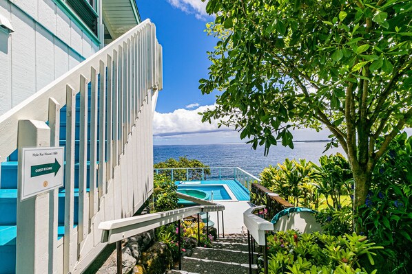 Guests enter through the hotel's inviting entrance, where a staircase leads to the rooms and a pool area offers a glimpse of the surrounding waters.