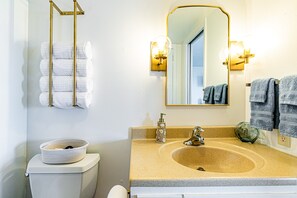 A bathroom with a beige sink, a gold towel rack, and a mirror with wall sconces. - Oceanfront in Hilo Hale Kai Suites - Moana Room - King Bed, Private Bathroom (Hilo)