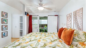 A bedroom with a bed, a ceiling fan, a door leading to a balcony, and a wall with framed artwork.