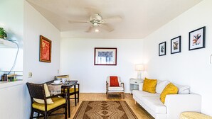 A living room with a white sofa, a dining table with chairs, a patterned rug, and wall art.