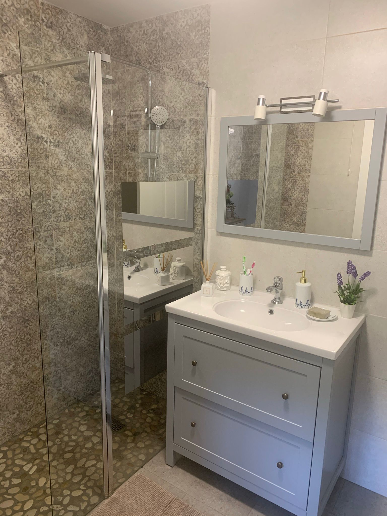 A bathroom with a glass shower enclosure, a vanity with a mirror, and a sink.