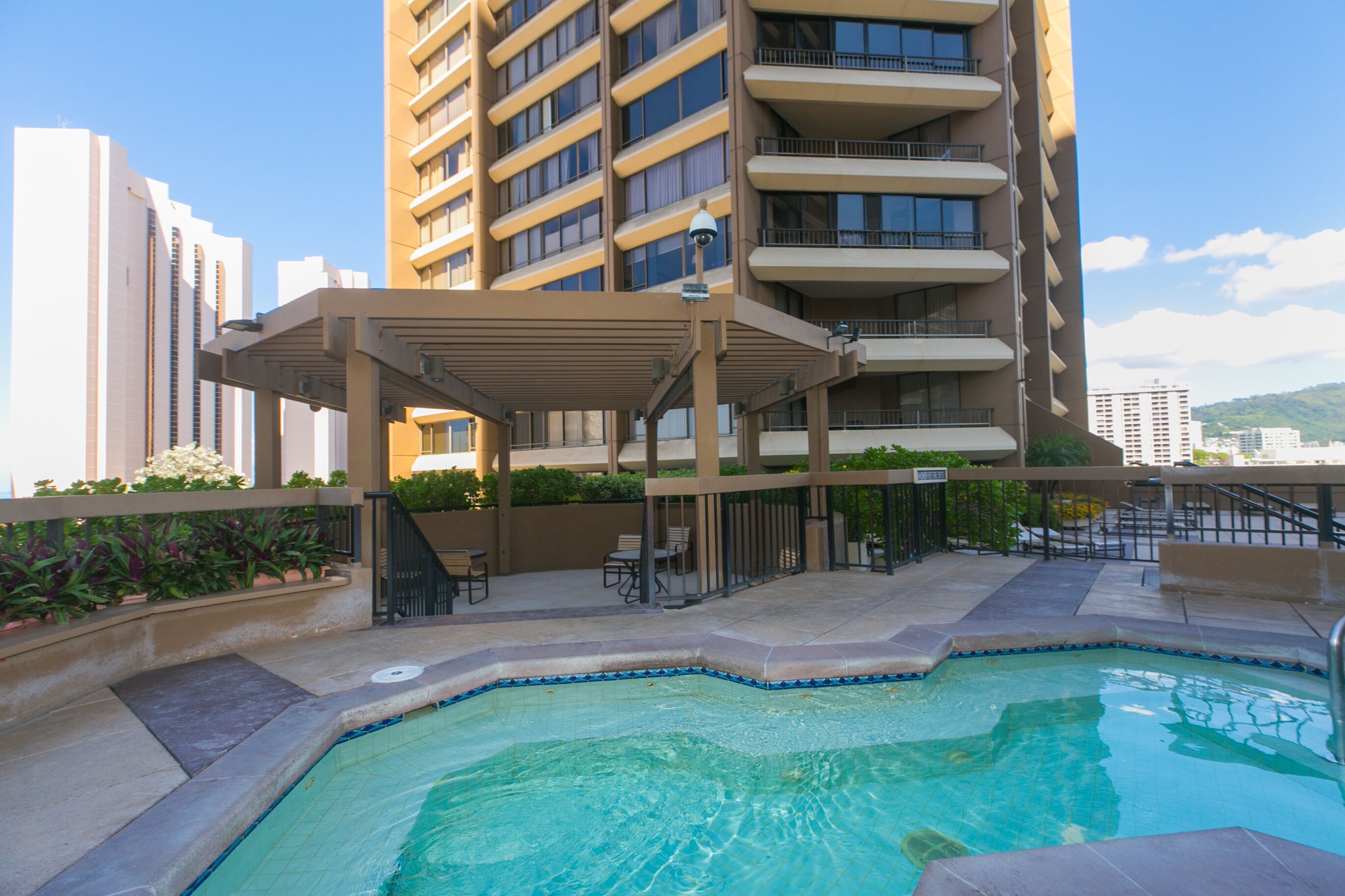 A rooftop pool area with a covered seating area, surrounded by a high-rise building with multiple balconies.