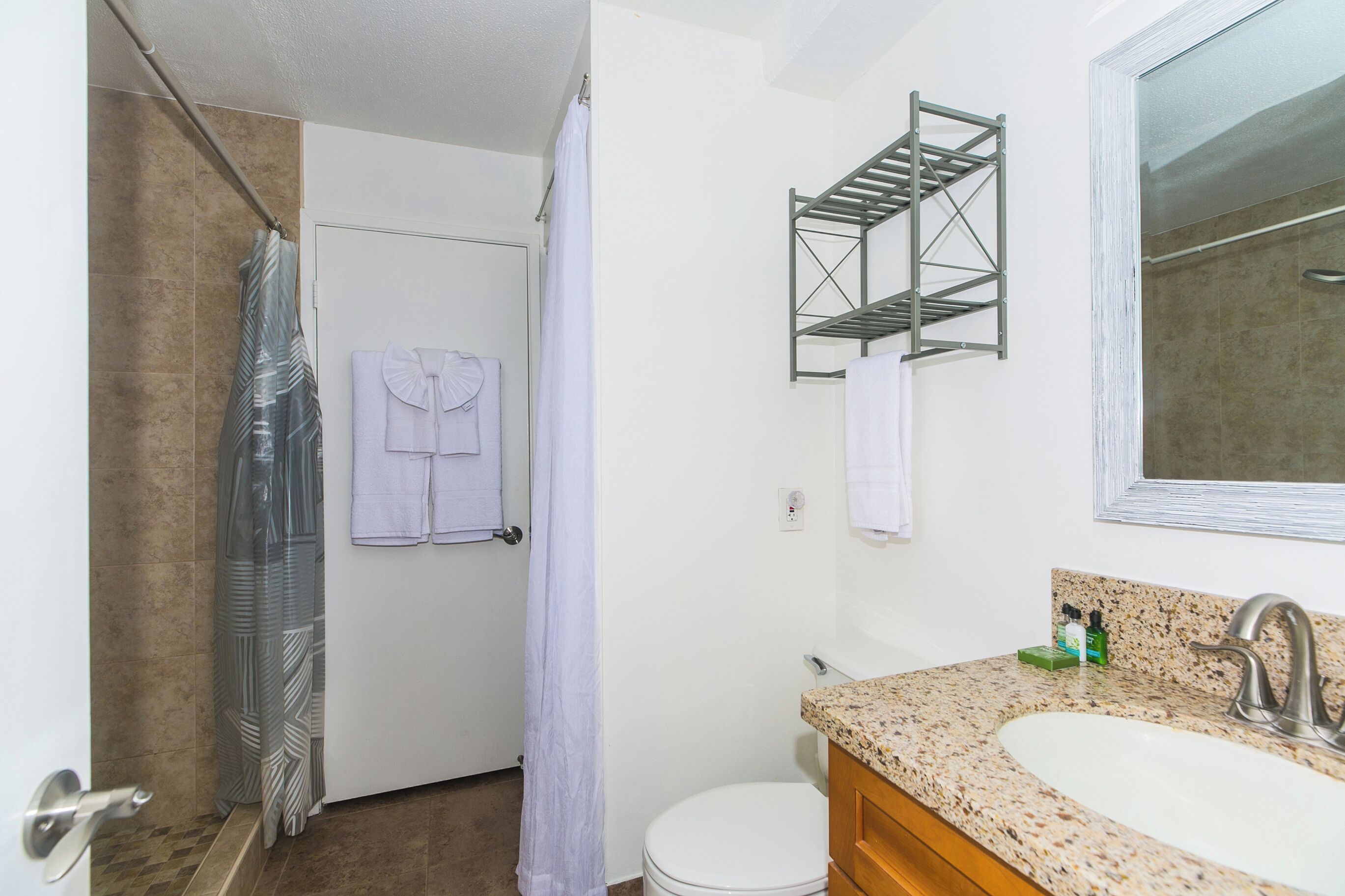 Une salle de bain comprenant une douche, des toilettes, un lavabo avec un plan de travail en granit et un porte-serviettes avec deux serviettes.