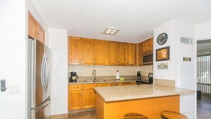 Eine Küche mit Holzschränken, einem Edelstahlkühlschrank, einer Granitabdeckung und zwei hölzernen Barhocker.