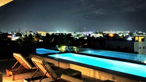 Ein Poolbereich auf dem Dach mit Liegestühlen und Blick auf die beleuchtete Stadt.