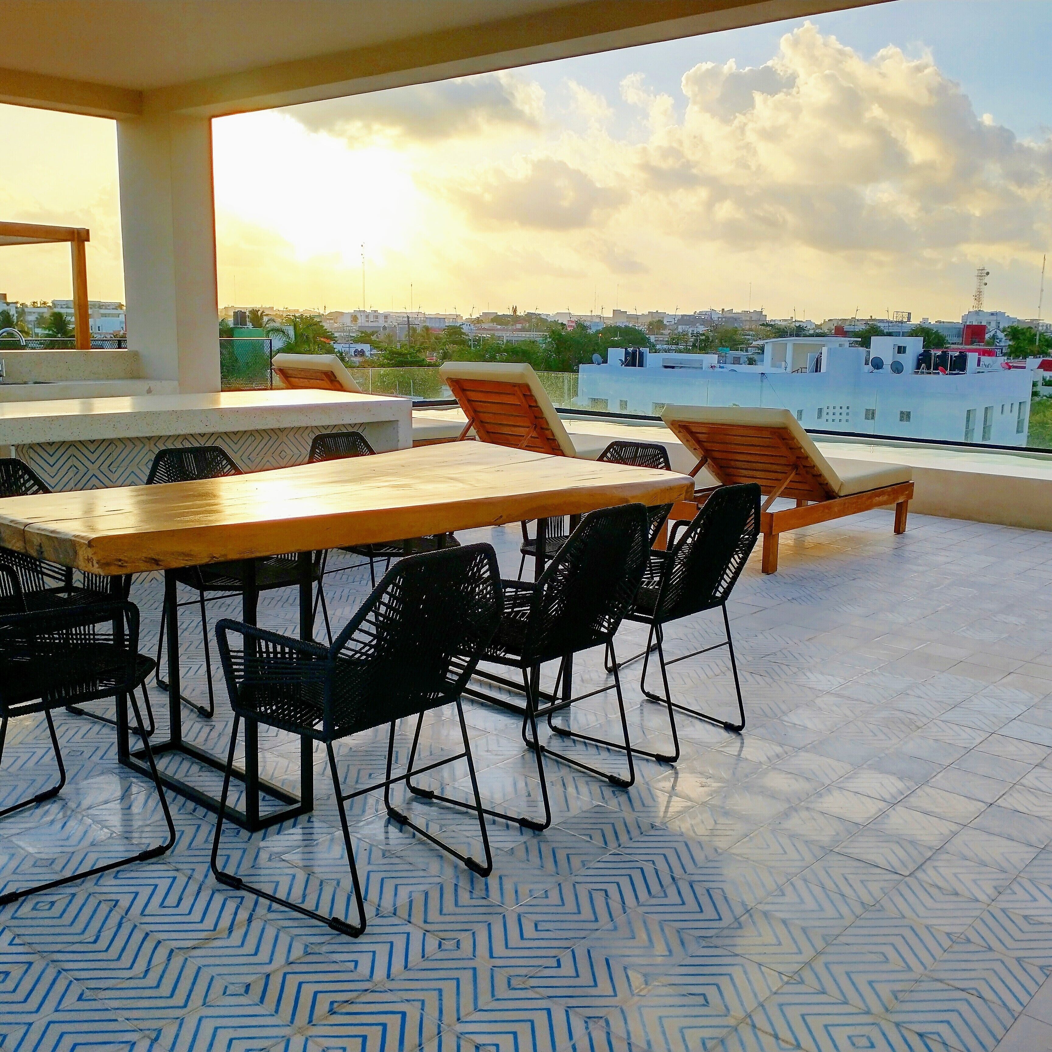A rooftop terrace with a dining table and chairs, a view of the cityscape, and a patterned floor.