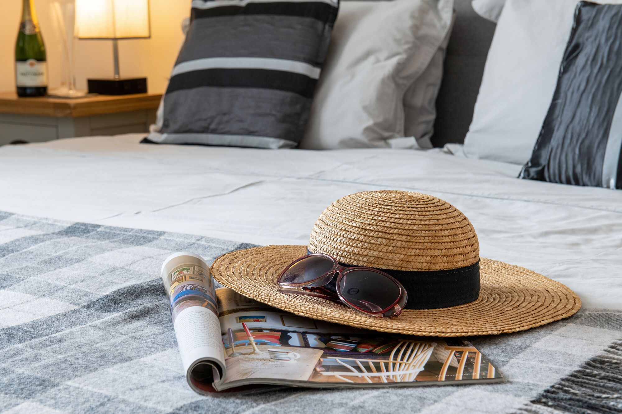 A bed with a checkered bedspread, a straw hat, sunglasses, and a magazine on it.