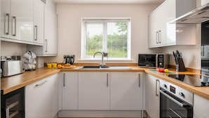 Una cocina moderna con armarios blancos, encimera de madera, un lavabo, un tostador, un hervidor, un microondas y un horno.