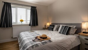 Un dormitorio con cama, mesita de noche, lámpara, ventana con cortinas y radiador.