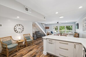 Une cuisine spacieuse avec un grand îlot central, un coin repas avec une table et des chaises, des meubles en osier et un escalier menant à un balcon.