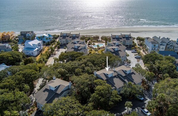 Vista aérea de uma área residencial costeira com várias casas de dois andares, uma piscina e uma praia ao fundo.