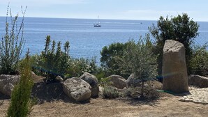 Eine Küstenlandschaft mit felsigem Vordergrund, einem großen Felsen und einem Segelboot auf dem Wasser.