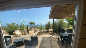 Eine Terrasse mit Gartenmöbeln, einem Tisch und Stühlen mit Blick auf Strand und Grünflächen.