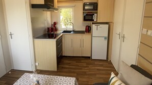 Eine kompakte Küchenzeile mit Mikrowelle, Herd und Kühlschrank. Ein kleiner Essbereich mit Tisch und einer Couch ist ebenfalls vorhanden.