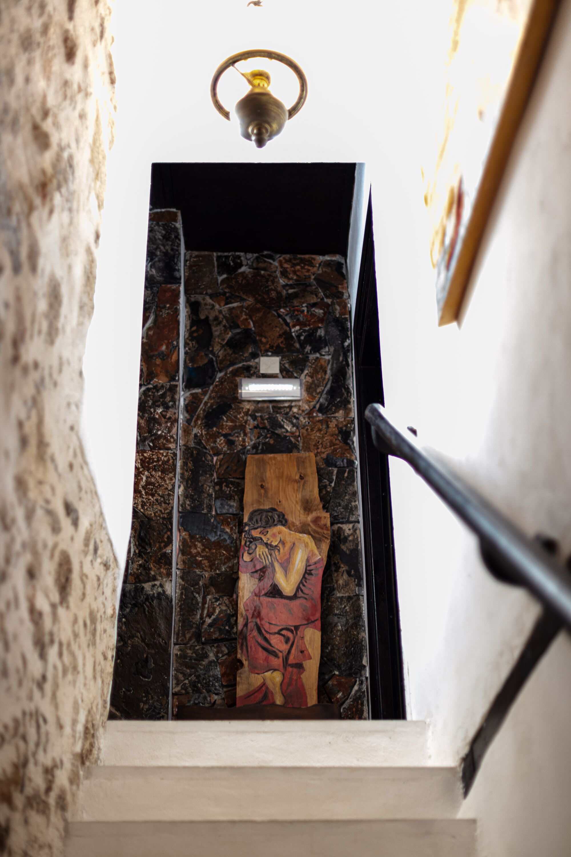 A staircase with a stone wall and a wooden panel with a painting.