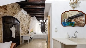 A bedroom with a stone wall, a wooden door, a bed with a canopy, a white chair, and a bedside table. - Antonia's rustic house - Old town view (Ρέθυμνο)