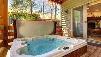 A hot tub in a wooden deck area with a view of trees and a stone fireplace.