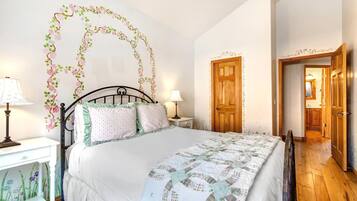 A bedroom with a bed, two bedside tables, a nightstand, a wooden door, and a hallway leading to a bathroom.