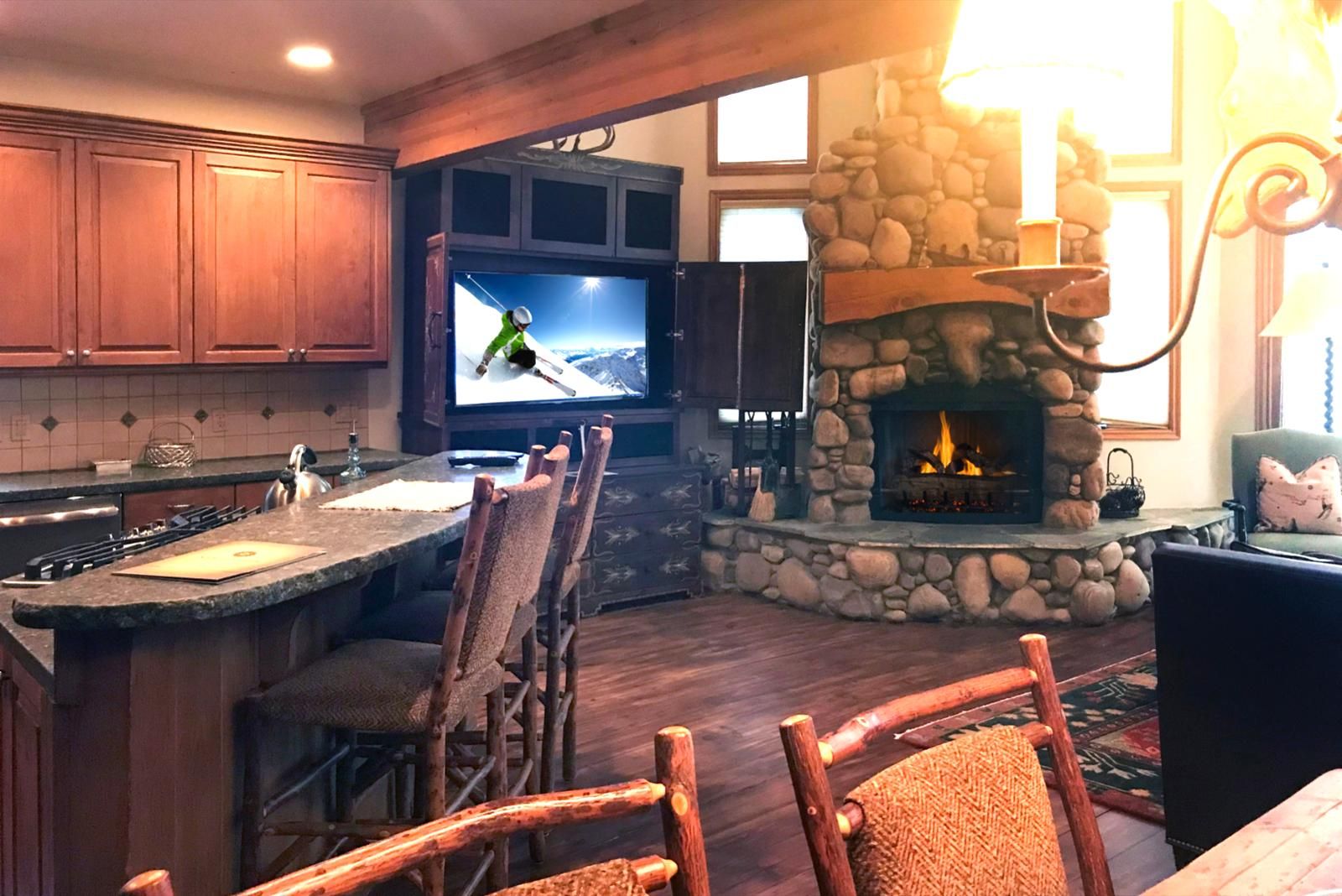 A kitchen with a stone fireplace, wooden cabinets, and a TV mounted above the counter.