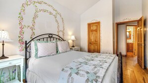 Een slaapkamer met een bed, twee nachtkastjes, een houten deur en een gang naar een badkamer.