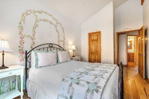 Una camera da letto con un letto, due comodini, una porta in legno e un corridoio che conduce al bagno.