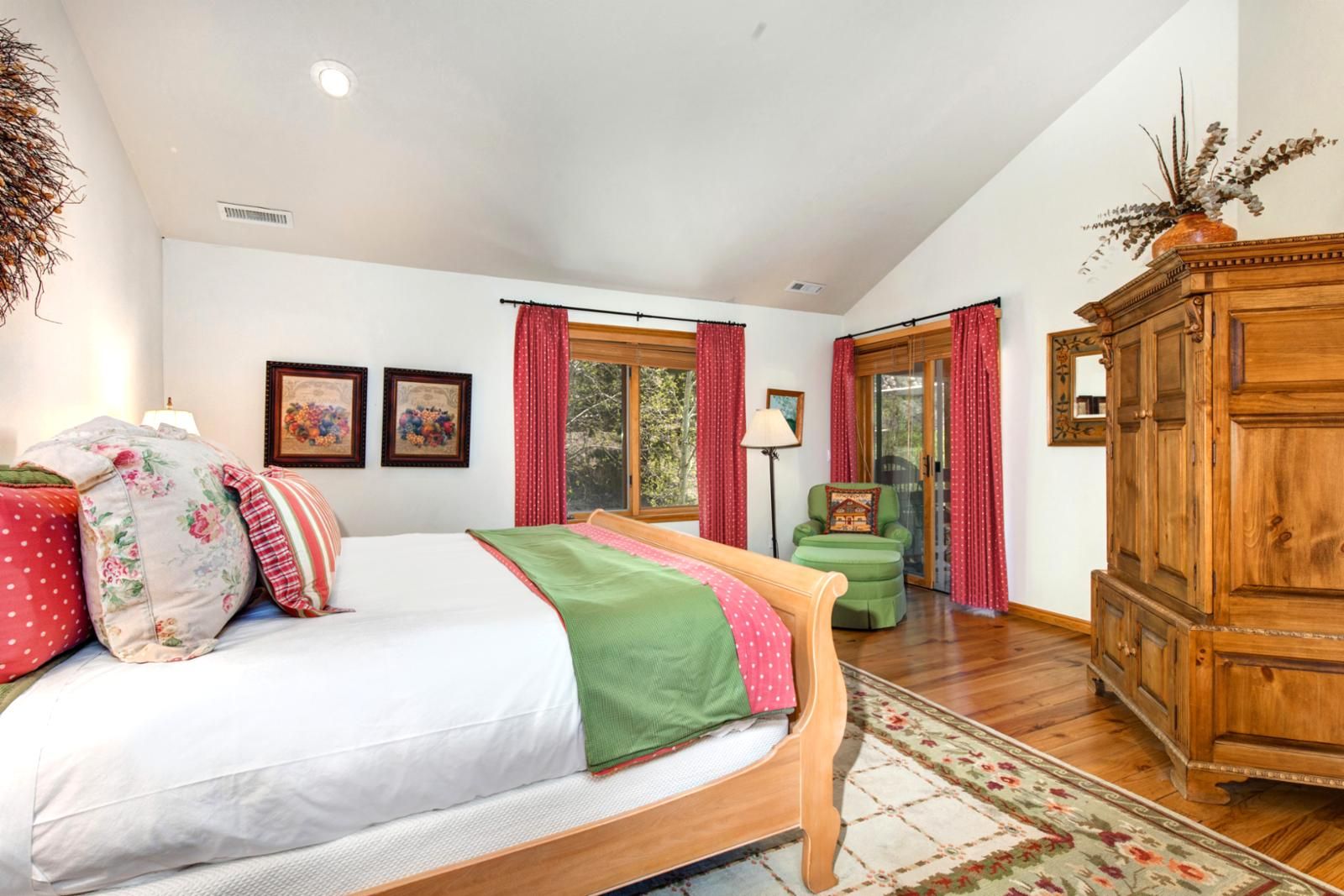 A bedroom with a bed, a wooden wardrobe, a green armchair, and a window with curtains.