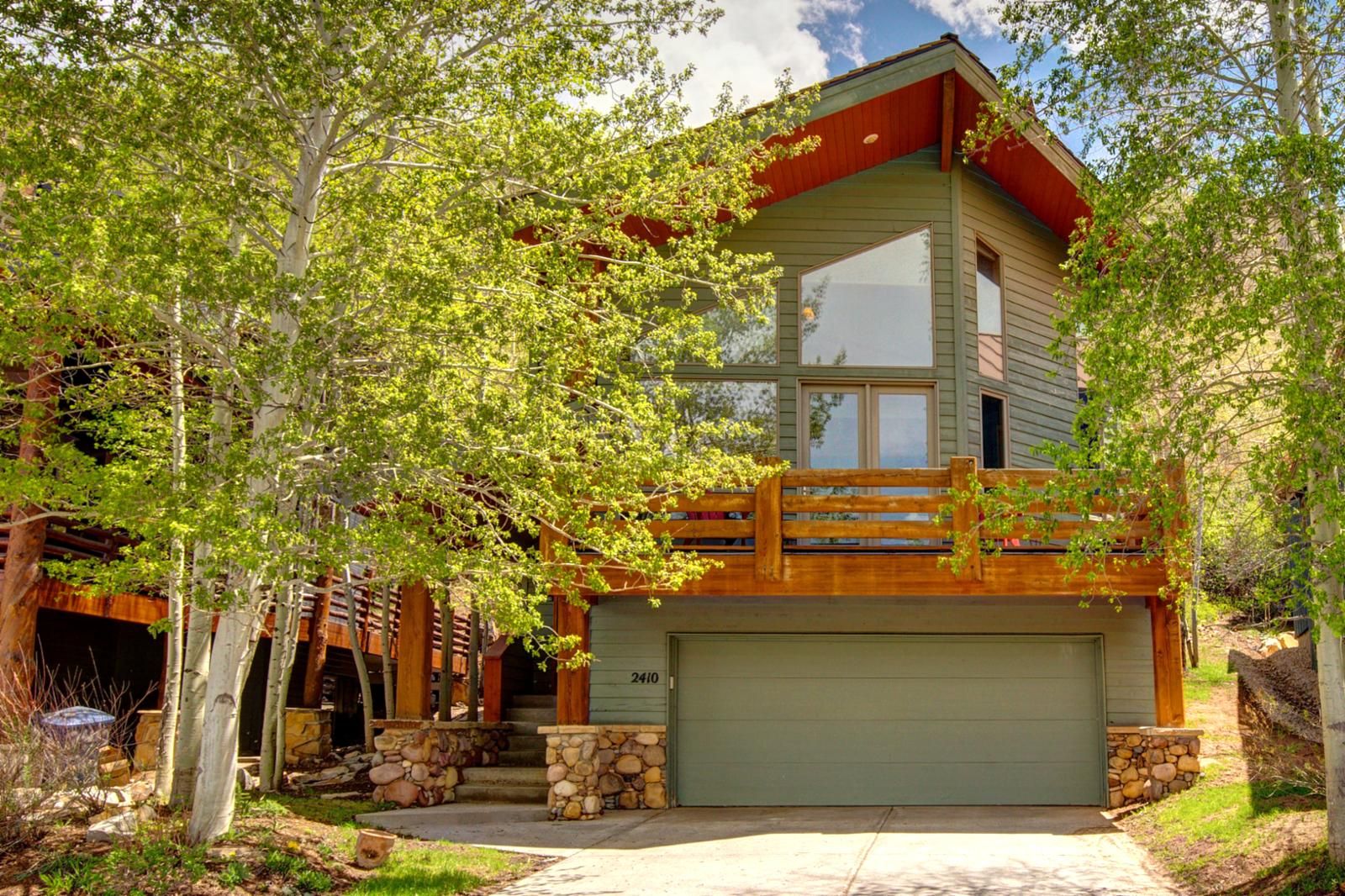 A two-story log cabin with a stone foundation, a large garage, and a wooden deck.