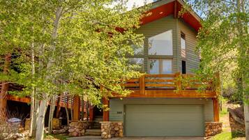 A two-story log cabin with a stone foundation, a large garage, and a wooden deck.